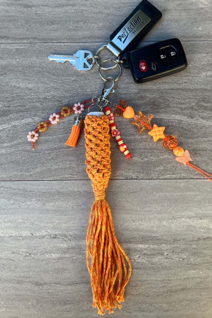 An orange macrame chapstick holder with beaded orange elements and an orange tassle keychain. Keychain charm